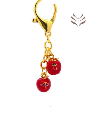 Close-up of red apple amulet with intricate ladybug and butterfly designs, gold chain and clasp, symbolizing peace and balance in feng shui.