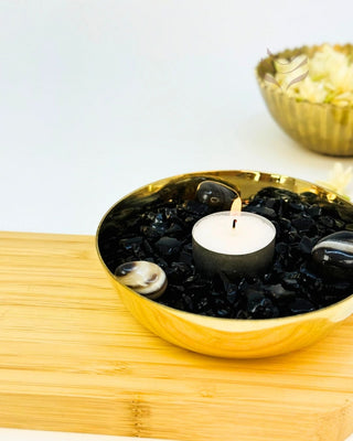 Crystal bowl with candle and black stones on wooden surface